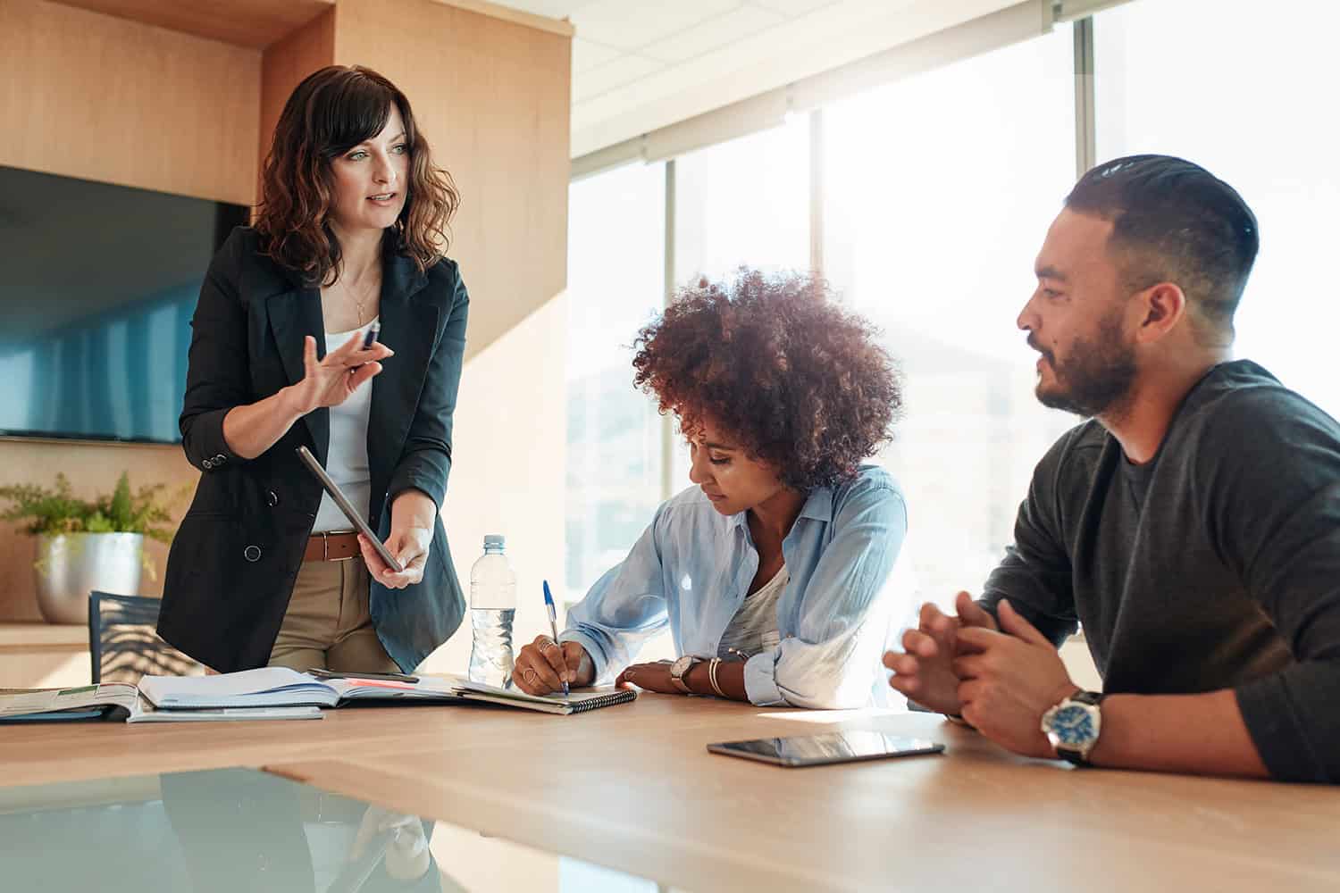 Young businesswoman showing something to her colleagues during a meeting in conference room during a regular check in.