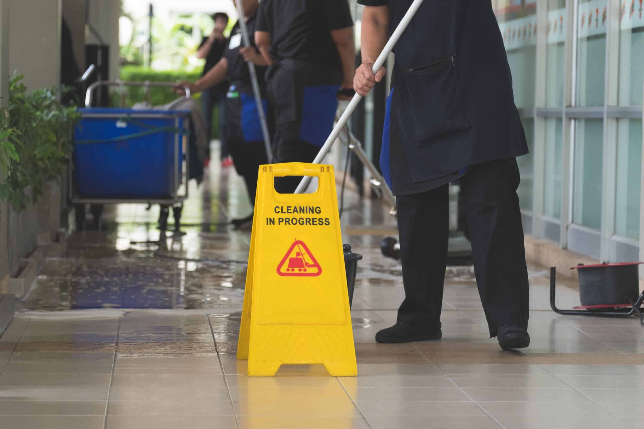 Woman mopping tiled floor behind a yellow wet floor sign