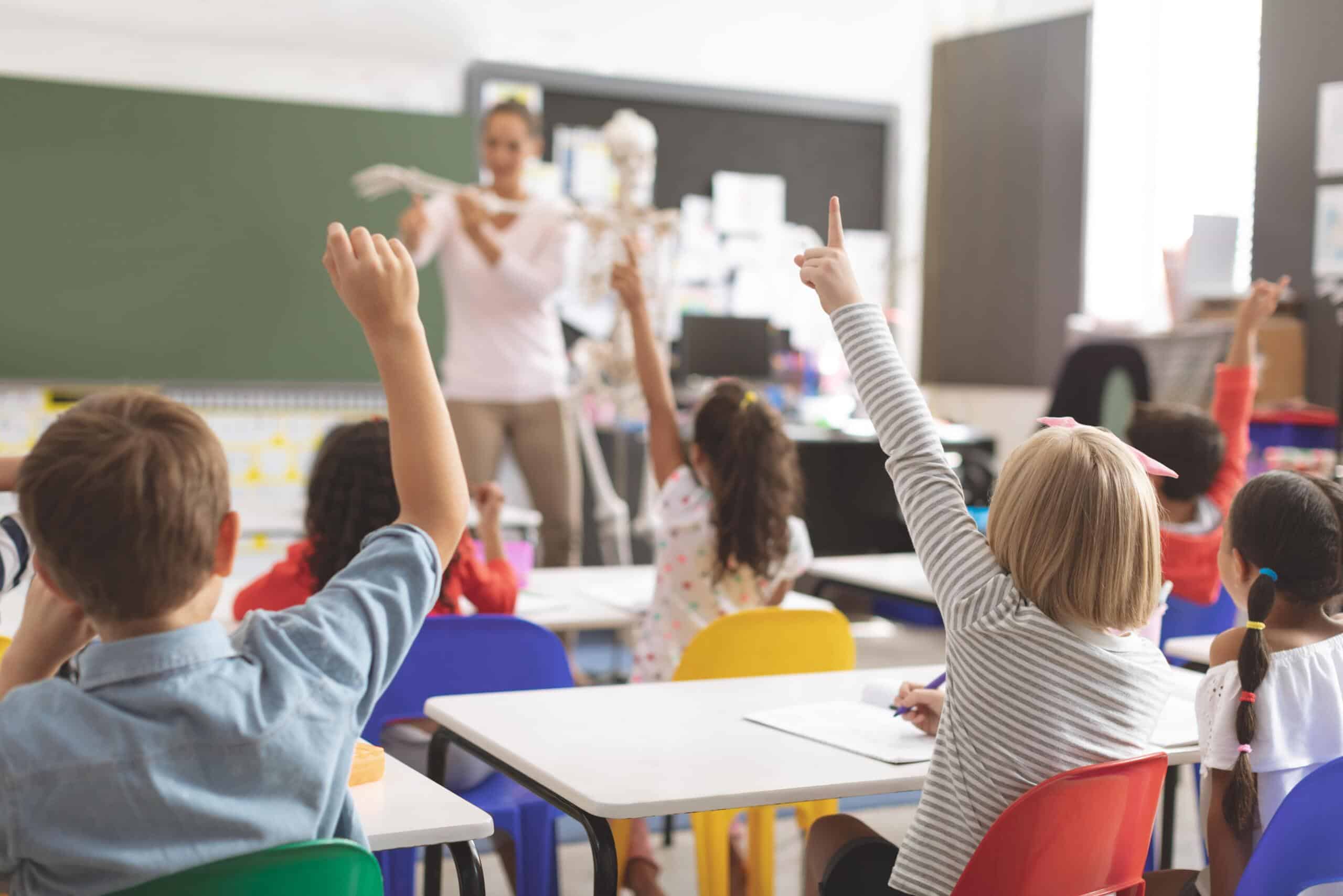 Children facing teacher with their hands up in a clean classroom