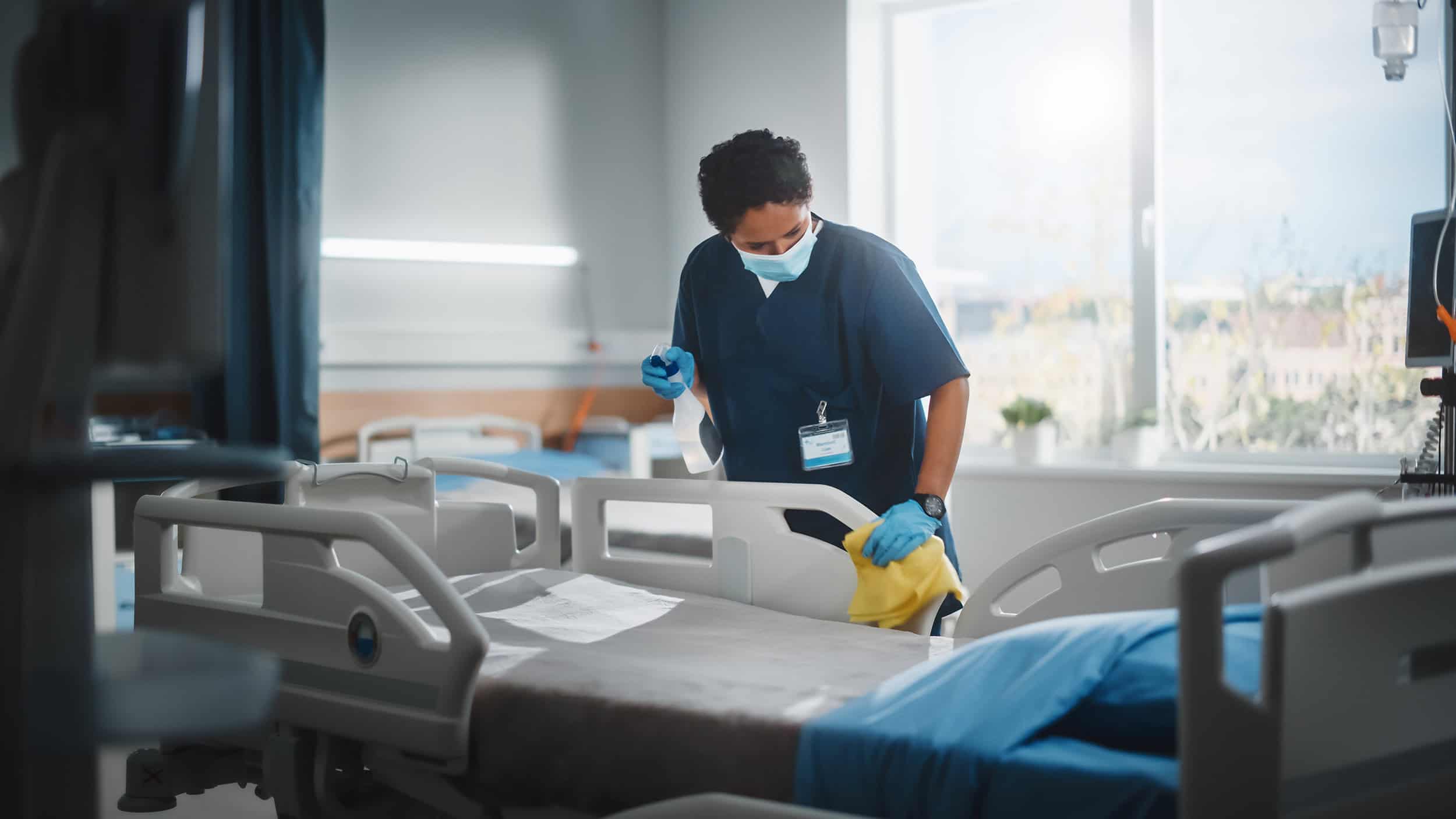 Commercial Cleaning Service Gold Coast Male cleaner in blue scrubs and yellow gloves santising hospital bed rail