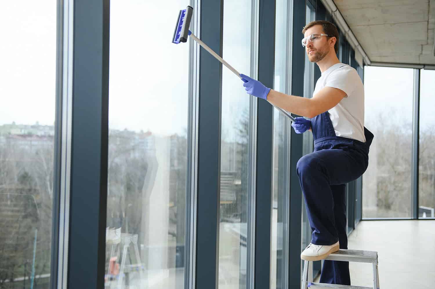 Cleaner wearing blue overalls and blue gloves washing shopping centre windows