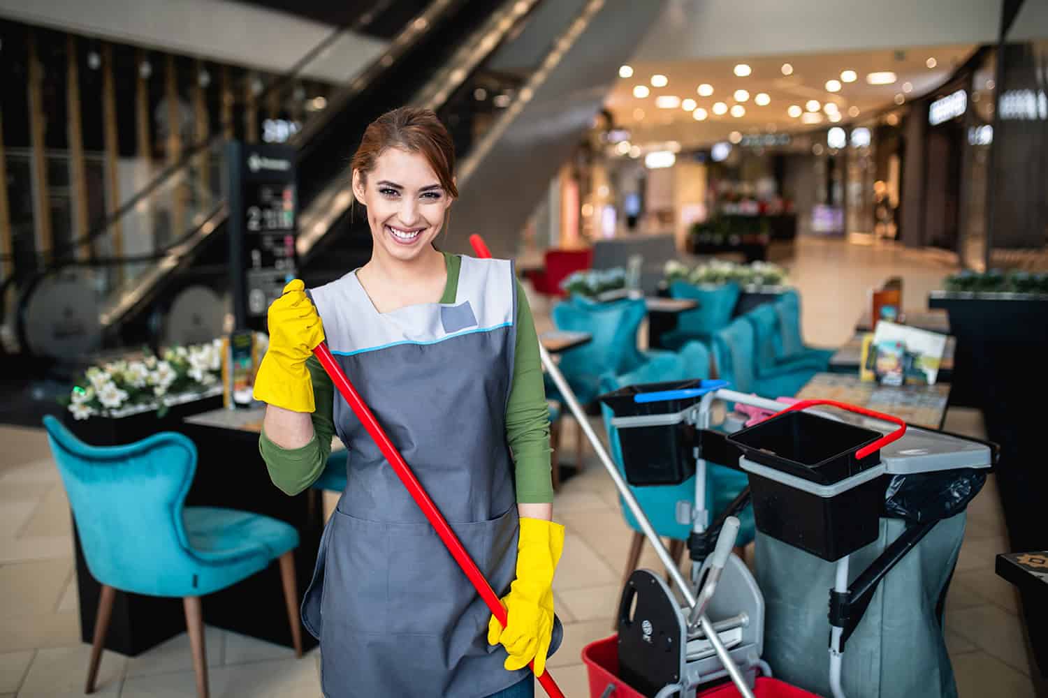 Cleaner wearing yellow gloves holding mop in a shopping centre food court