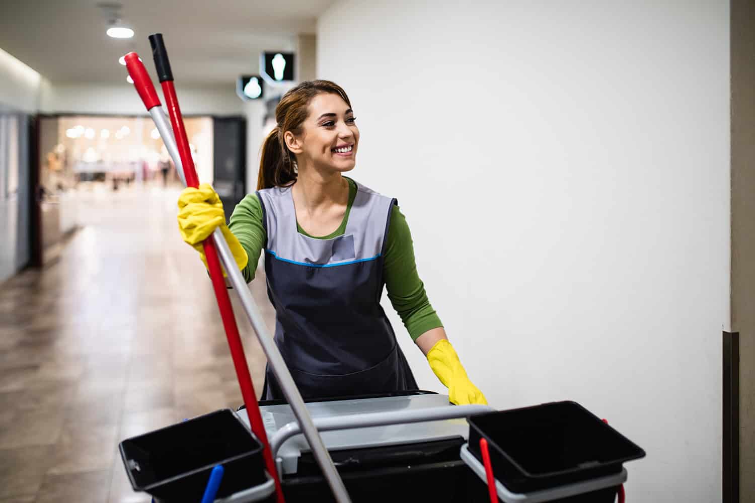 Cleaner wearing yellow rubber gloves wheeling cleaning equipment through shopping centre