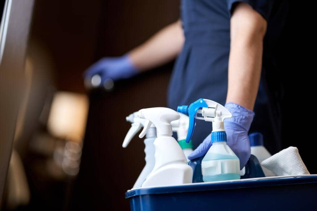 Cleaner with basket of anti-bacterial and sanitising cleaning products in spray bottles