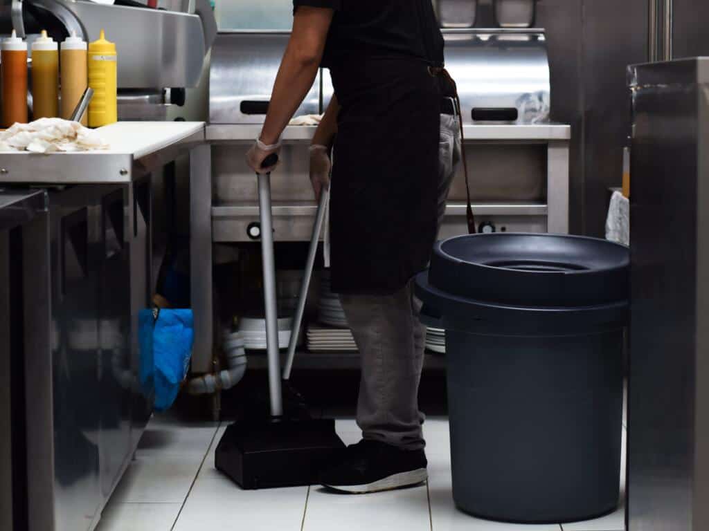 Man sweeping kitchen with long handled dustpan