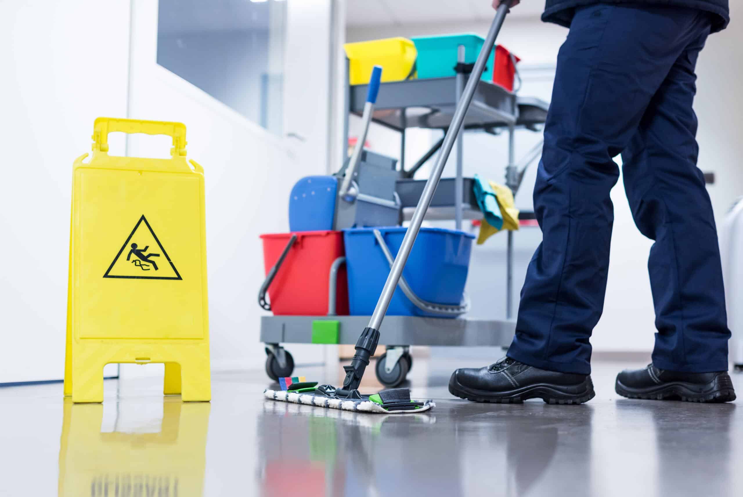 cleaner mopping the floor in front of a wet floor sign