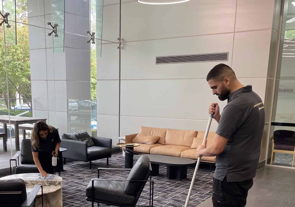 Two cleaning professionals doing cleaning services in an office area.